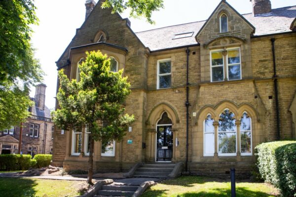 Stone stairs that lead to a big stone house that has been converted into flats surrounded by well looked after grass, trees and hedges.